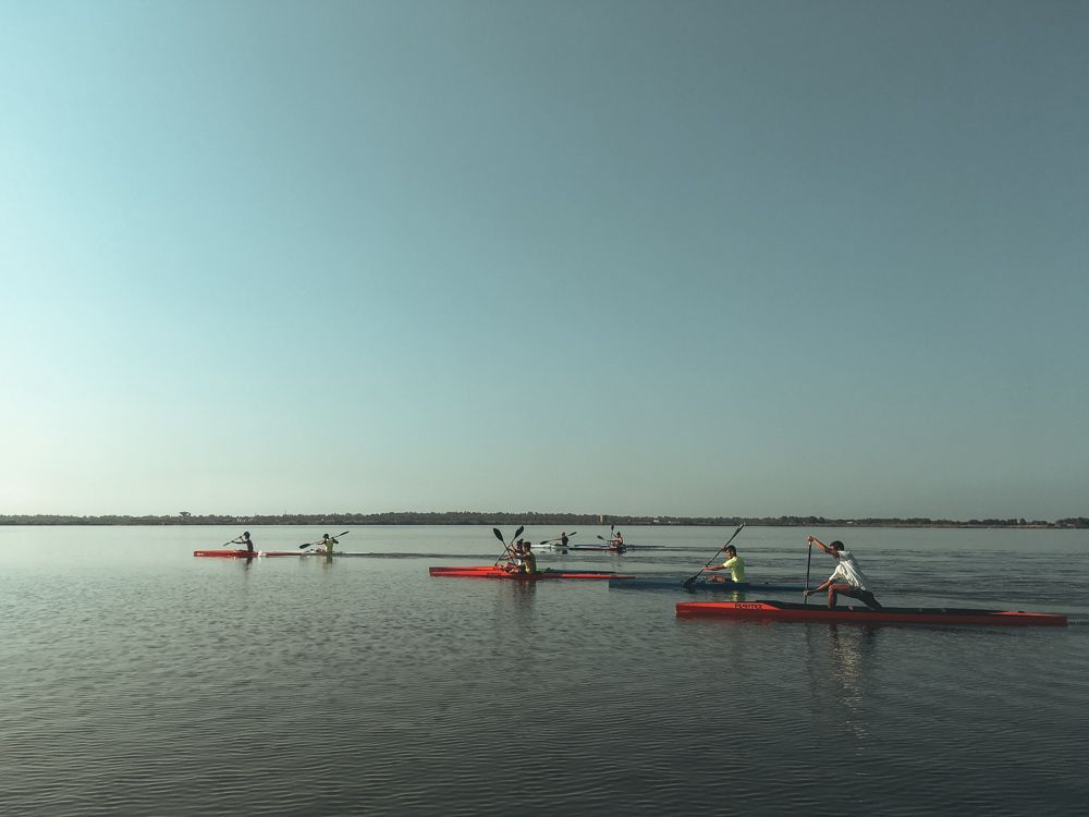 Gruppo di canoe sullo Stagno di Cabras al tramonto, cielo pastello e orizzonte piatto