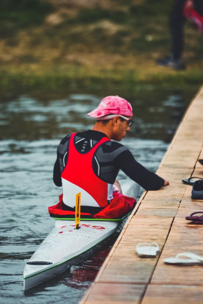 Atleta con canottiera rossa e nera in kayak accanto al pontile di legno