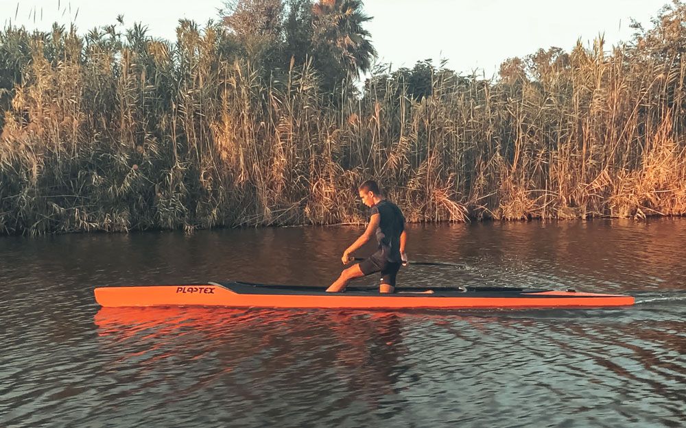 Un atleta in canoa canadese arancione sullo Stagno di Cabras davanti al canneto dorato, luce del tardo pomeriggio